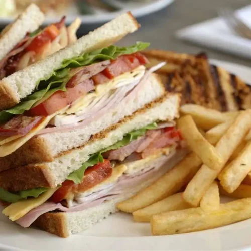 Club sandwich and fries served on a white plate with pickles